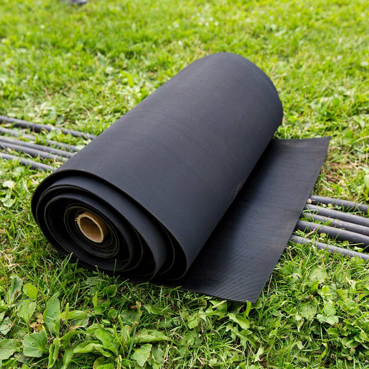 Rolle einer schwarzen Kabelschutzmatte aus Gummi, teilweise ausgerollt auf einer Wiese liegend und darunter Kabel