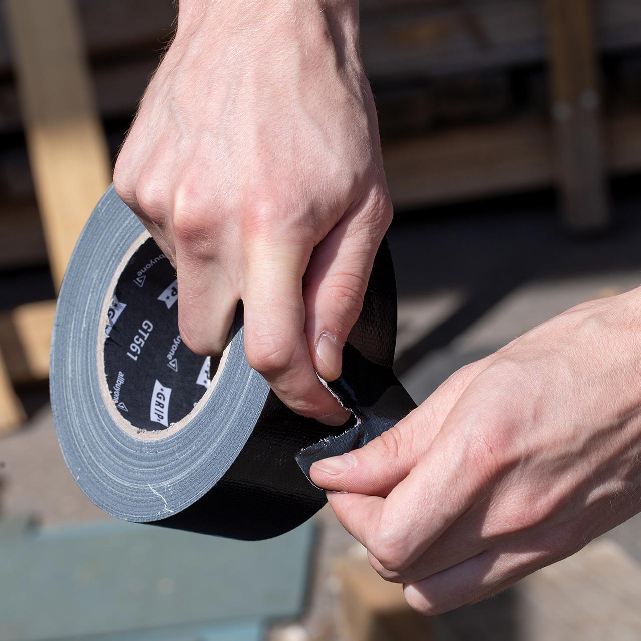 Hände reißen schwarzes Gewebeklebeband mit sauberer Abrisskante quer von der Rolle