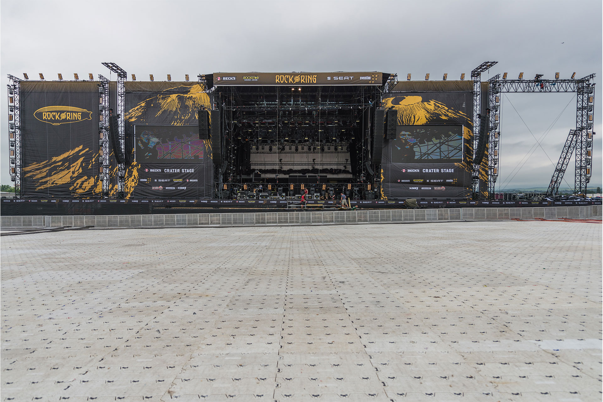 Bühne mit Header und beidseitiger schwarzer PVC Vollplane als Verkleidung mit gelben Grafiken während Festivalaufbau