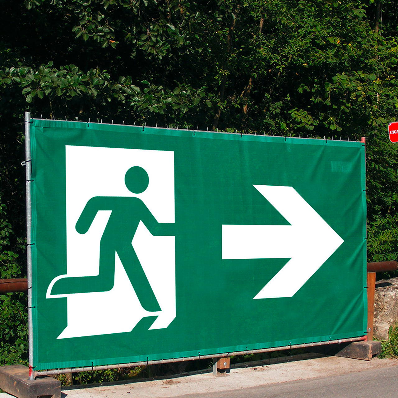 Notausgangsbanner mit Pfeil nach rechts, befestigt an einem Bauzaunelement vor dichtem Baumbewuchs