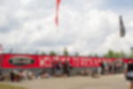 Frontlit PVC - Zaunbanner als Werbung und Branding für Events Geöstes rotes Frontlit PVC Banner mit weißem Schriftzug und Logo an einem Zaun mit Festivalbesuchern davor